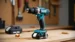 A Makita XFD131 brushless drill with a battery on a wooden workbench, with wood shavings nearby. The image highlights the compact design of the cordless tool. Tested on tool tested.