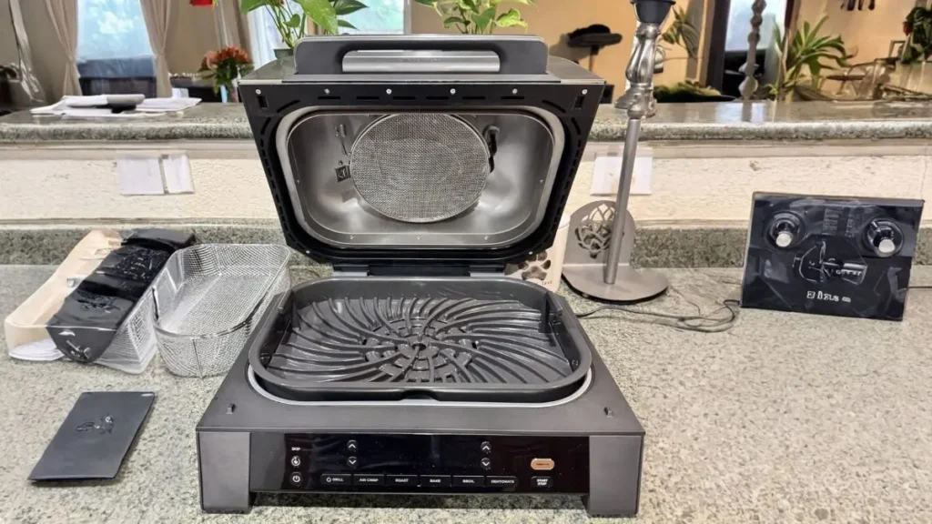 The Ninja Foodi grill with the lid open, showing the circular splatter shield and the heavy-duty grill grate.