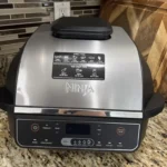 A sleek silver and black Ninja Foodi Smart XL 6-in-1 Indoor Grill sitting on a granite countertop, reviewed by Tool Tested.